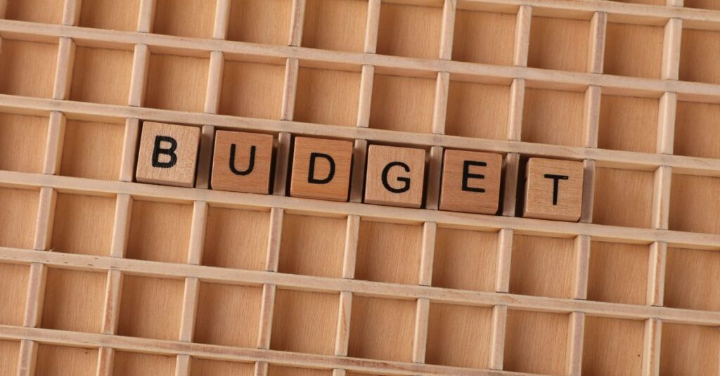 Holz-Scrabble-Buchstaben, die 'Budget' auf einem strukturierten Holzraster buchstabieren und finanzielle Planung symbolisieren.