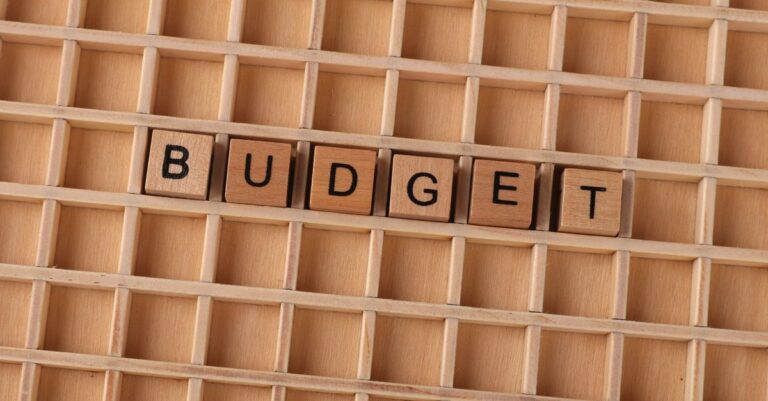Holz-Scrabble-Buchstaben, die 'Budget' auf einem strukturierten Holzraster buchstabieren und finanzielle Planung symbolisieren.