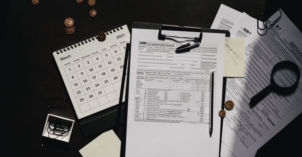 Ein ordentlich organisierter Arbeitsplatz mit Steuerformularen, Kalender, Lupe und Büromaterialien für eine effiziente Steuererklärung.