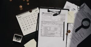 Ein ordentlich organisierter Arbeitsplatz mit Steuerformularen, Kalender, Lupe und Büromaterialien für eine effiziente Steuererklärung.