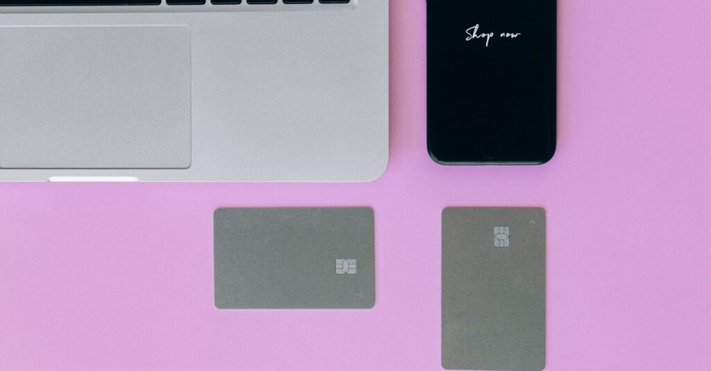 Laptop, Karten und Smartphone auf pinkem Hintergrund für Online-Shopping.