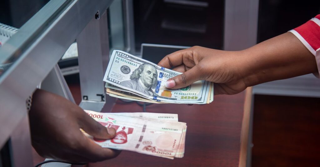 Hände tauschen US-Dollar und lokale Währung am Bankschalter, was internationale Finanzen symbolisiert.